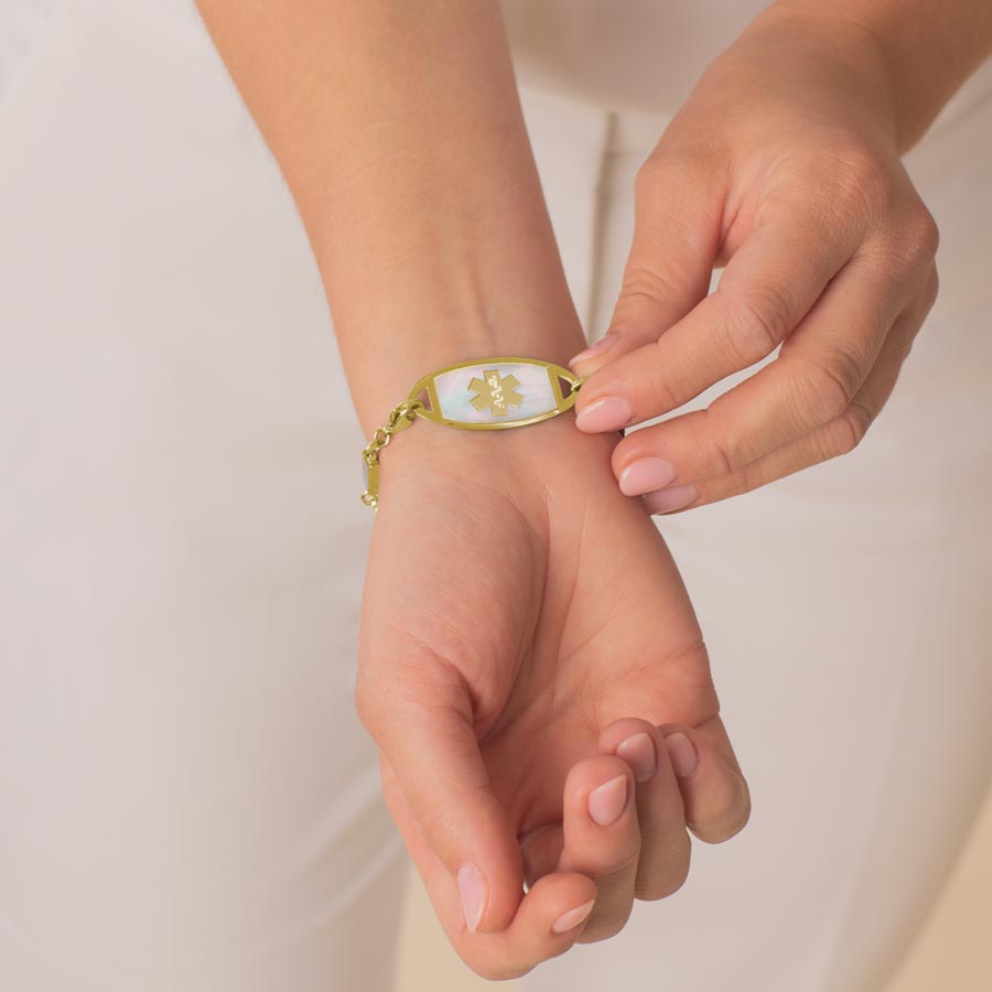 Woman showing decorative medical alert tag with mother of pearl inlay and yellow gold medical caduceus symbol