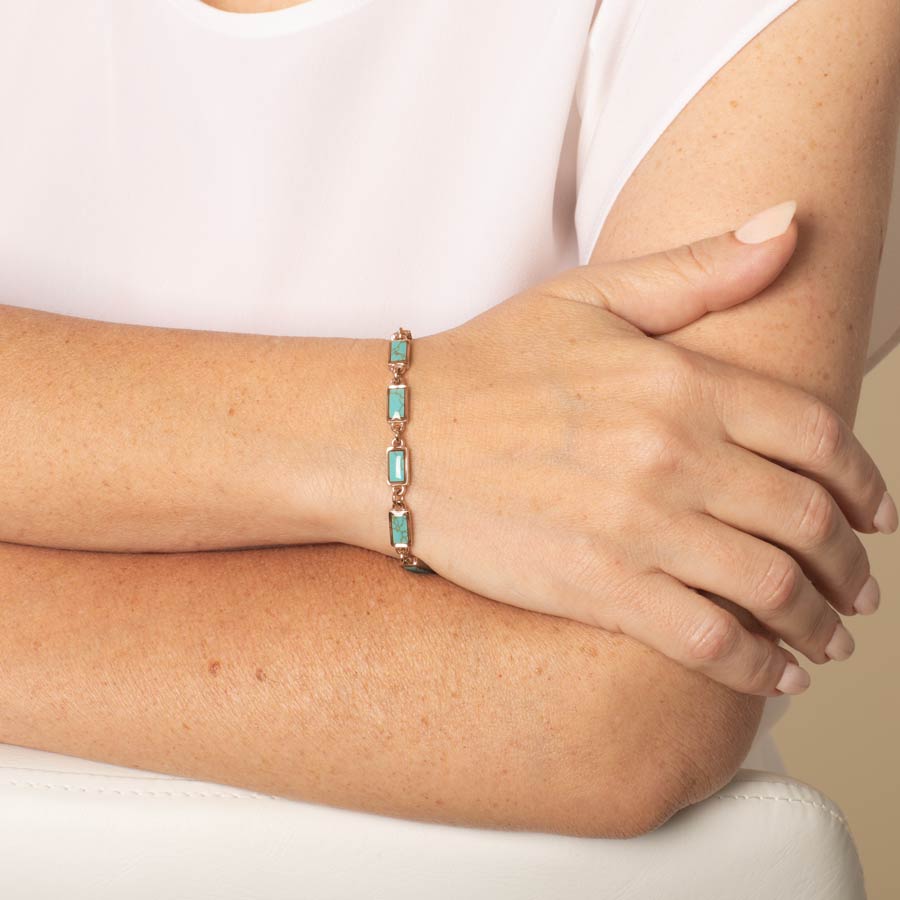 Woman with arms crossed wearing bracelet in turquoise and rose gold.