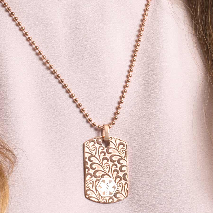 Woman wearing rose gold medical ID alert dog tag necklace with floral swirl pattern and white caduceus symbol