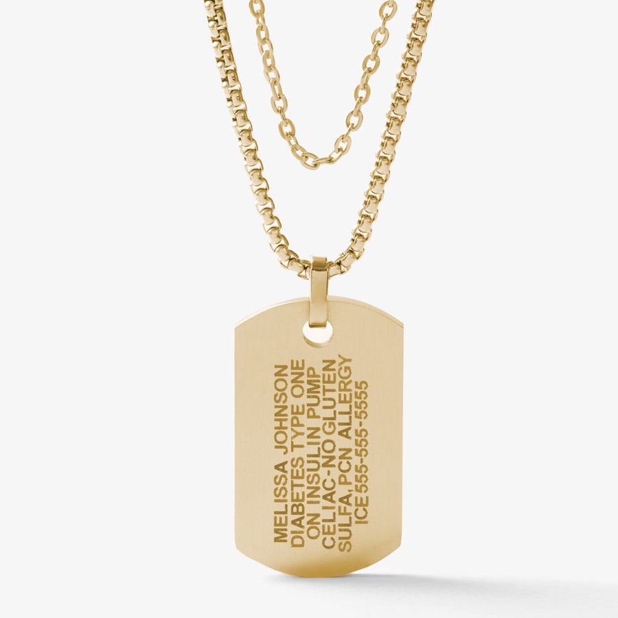 Back side of 14K gold tone medical ID dog tag on a gold tone snake chain layered with gold tone accent chain showing engraving example.