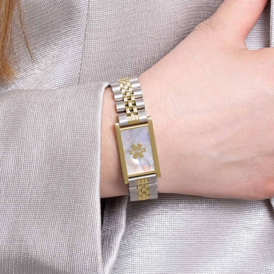 Woman wearing two tone silver and gold linked bracelet with mother of pearl inlay tag.