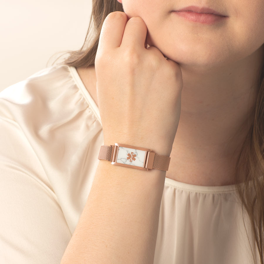 Woman with hand on face wearing rose gold medical ID bracelet with mesh band and howlite plate