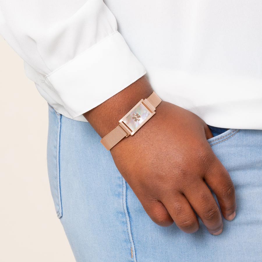 Woman wearing rose gold stainless steel mesh bracelet with rose gold tone ID tag with natural mother of pearl inlay.