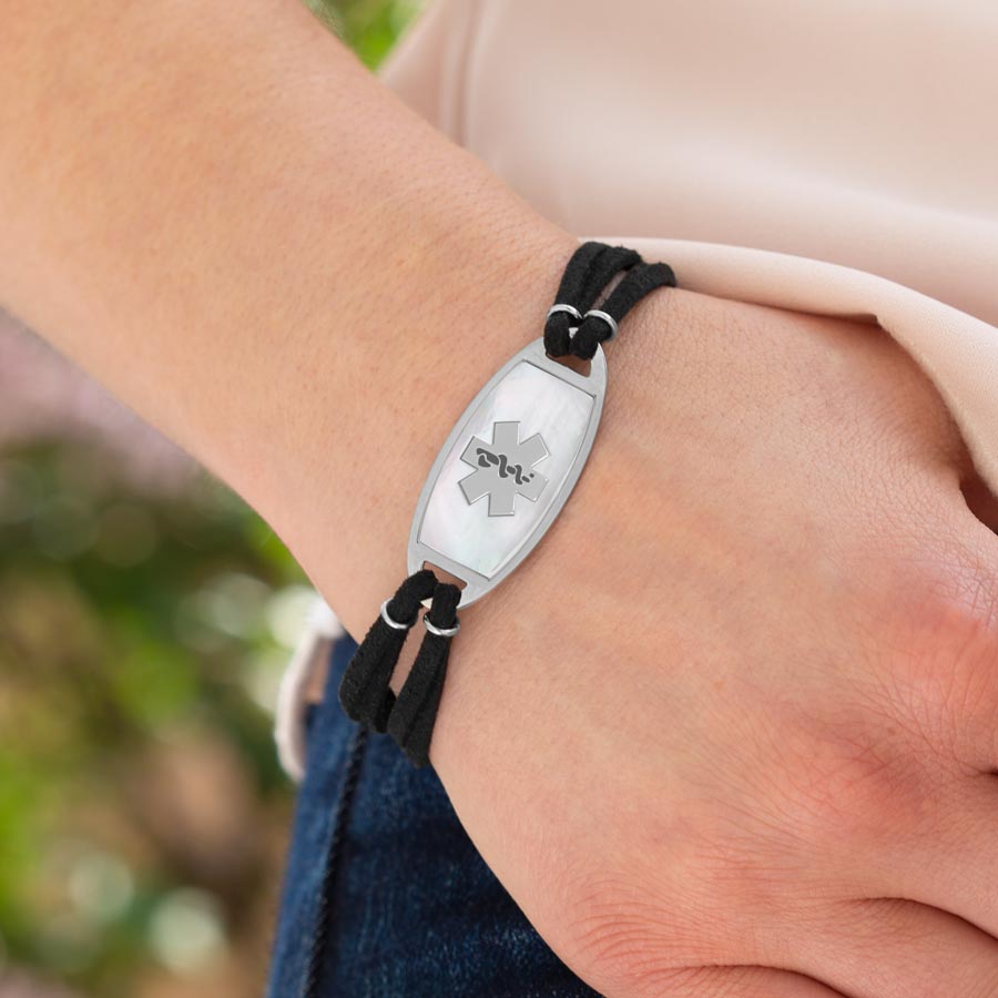 Woman wearing black faux suede medical ID bracelet with affixed stainless steel med ID tag with mother of pearl inlay.