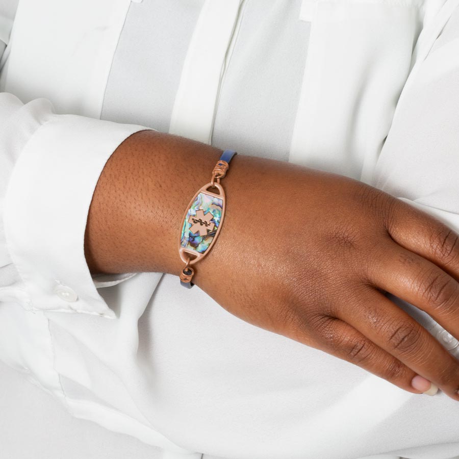 Woman wearing navy blue metallic leather medical ID bracelet with rose gold tone stainless steel medical ID tag with abalone inlay.