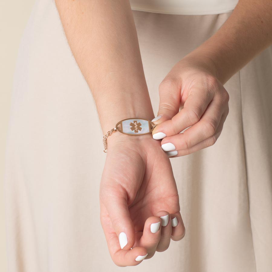 Woman wearing rose gold tone stainless steel medical ID tag with black paint inlay and rose gold tone medical symbol at the center.