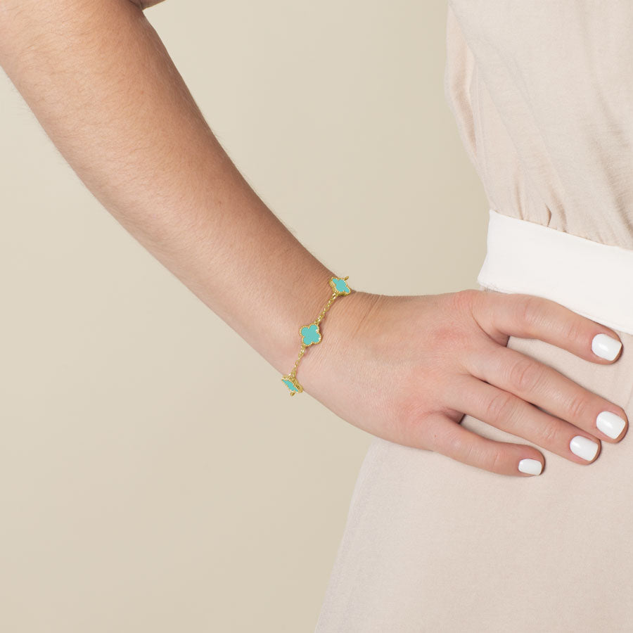 Model wearing a bracelet with 3 clover shaped links showing. The links are inlaid with turquoise paint.