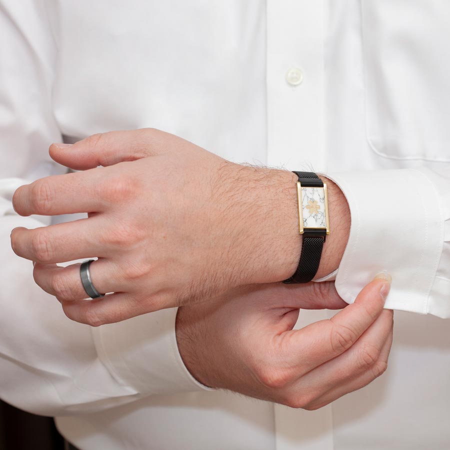 Man wearing black stainless steel, adjustable mesh band with magnetic clasp affixed to stainless steel medical ID tag with howlite inlay and coordinating silver tone medical symbol.