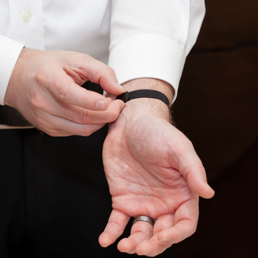 Man showing magnetic clasp on black stainless steel adjustable mesh band medical ID bracelet.