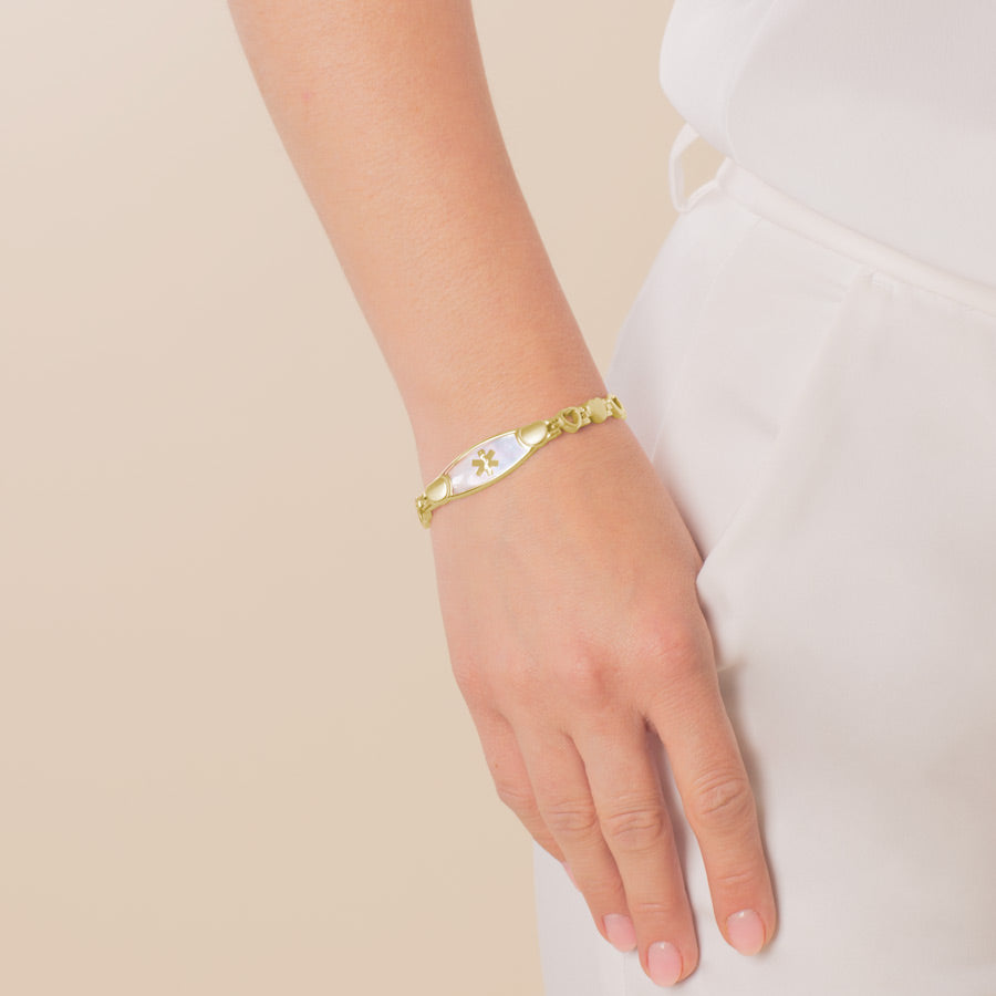 Woman wearing yellow gold tone linked medical alert bracelet with mother of pearl inlay