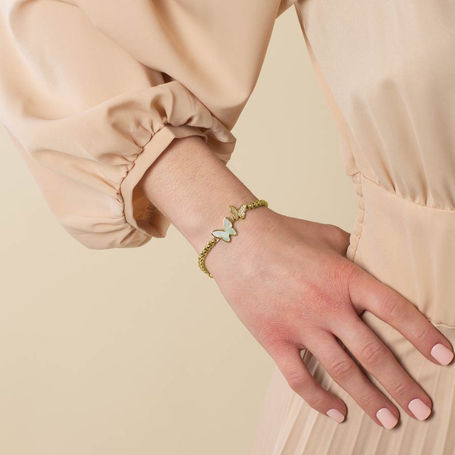 Woman wearing a gold tone box chain featuring a double butterfly centerpiece, inlaid with Mother of Pearl and cubic zirconia crystals.