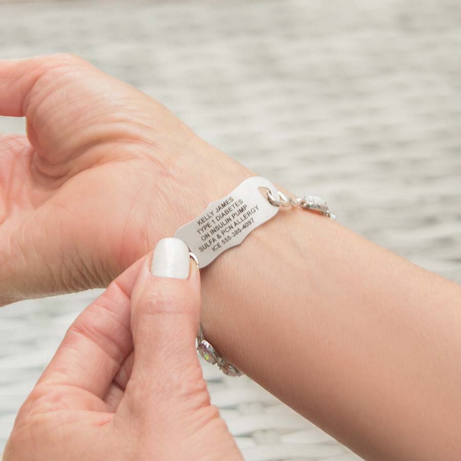 Woman showing engraving on the La Petite White Caduceus Medical ID Tag on the Opal Medical ID Bracelet in Sterling Silver