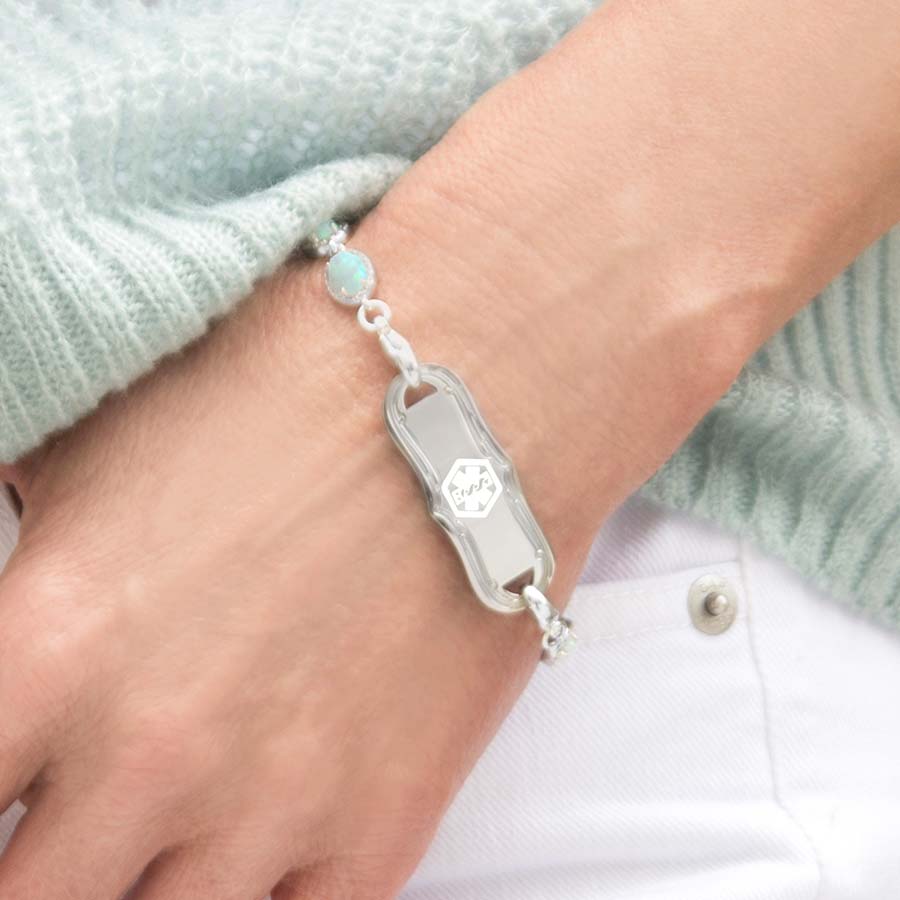 Woman wearing the La Petite White Caduceus Medical ID Tag on the Opal Medical ID Bracelet in Sterling Silver with opal links