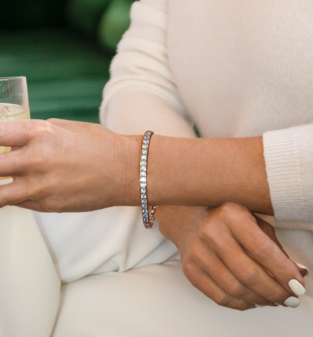 Woman in white holding glass wearing rose gold tone medical ID tennis bracelet with pave set cubic zirconia crystals.