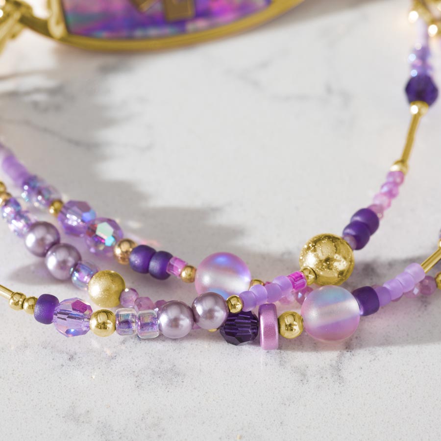 Close up of purple and gold beads on Jolie Medi ID Bracelet shown on white marble countertop