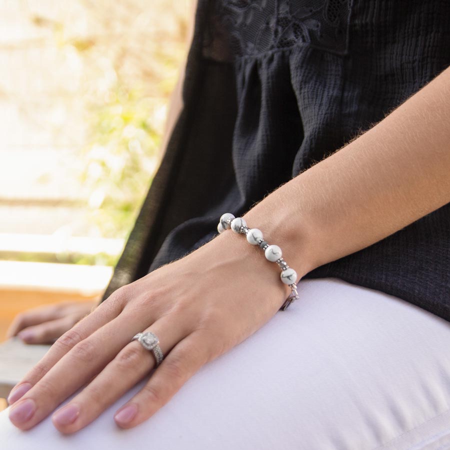 Woman wearing white marbled beaded stretch medical ID bracelet with hand on her lap.