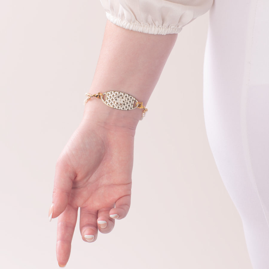 Woman showing gold medical ID tag with pearl inlay cross pattern