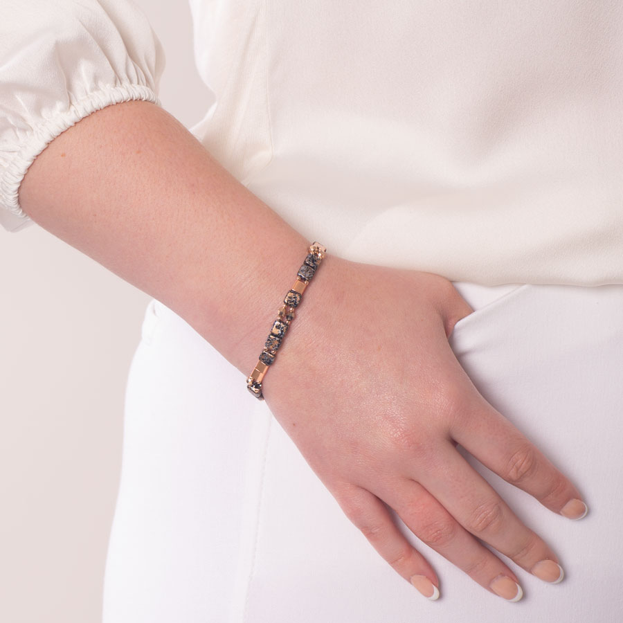 Woman in white top and pants wearing black, rose gold, and crystal beaded stretch bracelet.