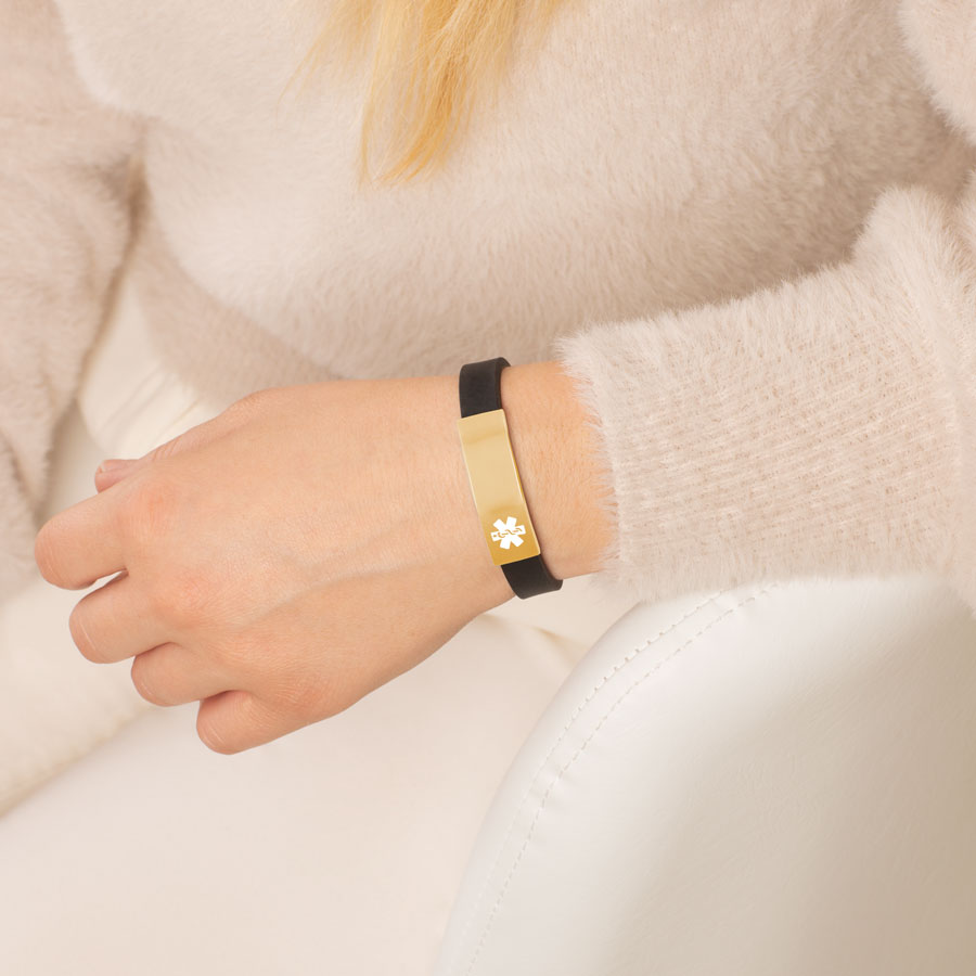 Woman wearing black silicone medical ID bracelet with gold tone stainless steel medical ID tag.