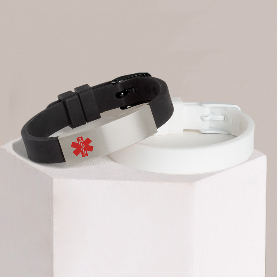 Black silicone medical ID bracelet with stainless steel medical alert tag stacked with white silicone medical alert bracelet on hexagon block.