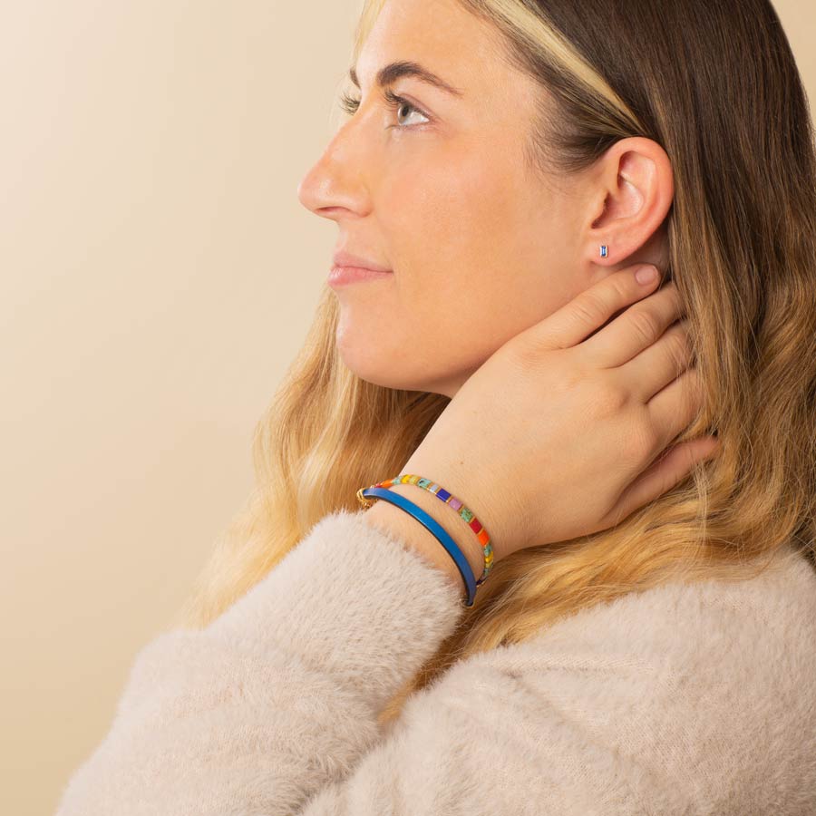 Woman wearing blue baguette earring with tropical colored beaded stretch bracelet layered with metallic blue leather bracelet.