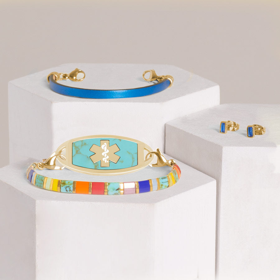 Tropical colored beaded stretch bracelet with a gold med ID tag inlaid with Turquoise, stacked with metallic blue leather bracelet and blue baguette earrings on hexagon blocks.