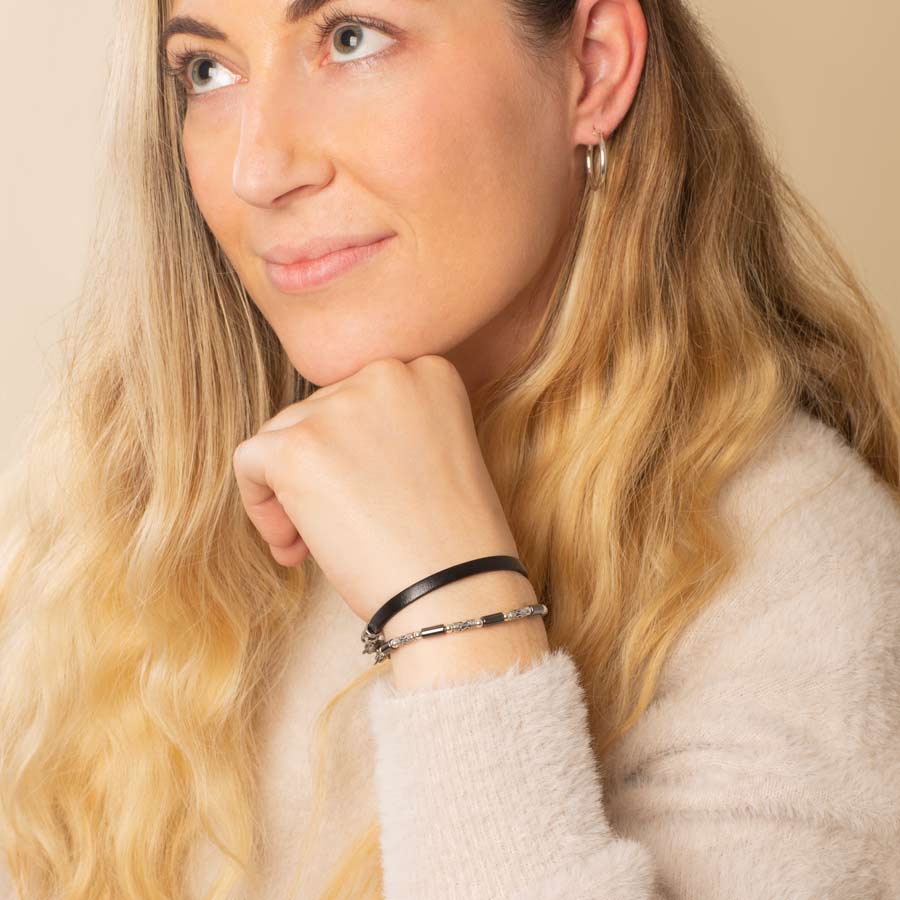 Woman wearing sterling silver bali beads and tubular hematite beaded bracelet layered with black leather bracelet and silver tone hoop earrings.