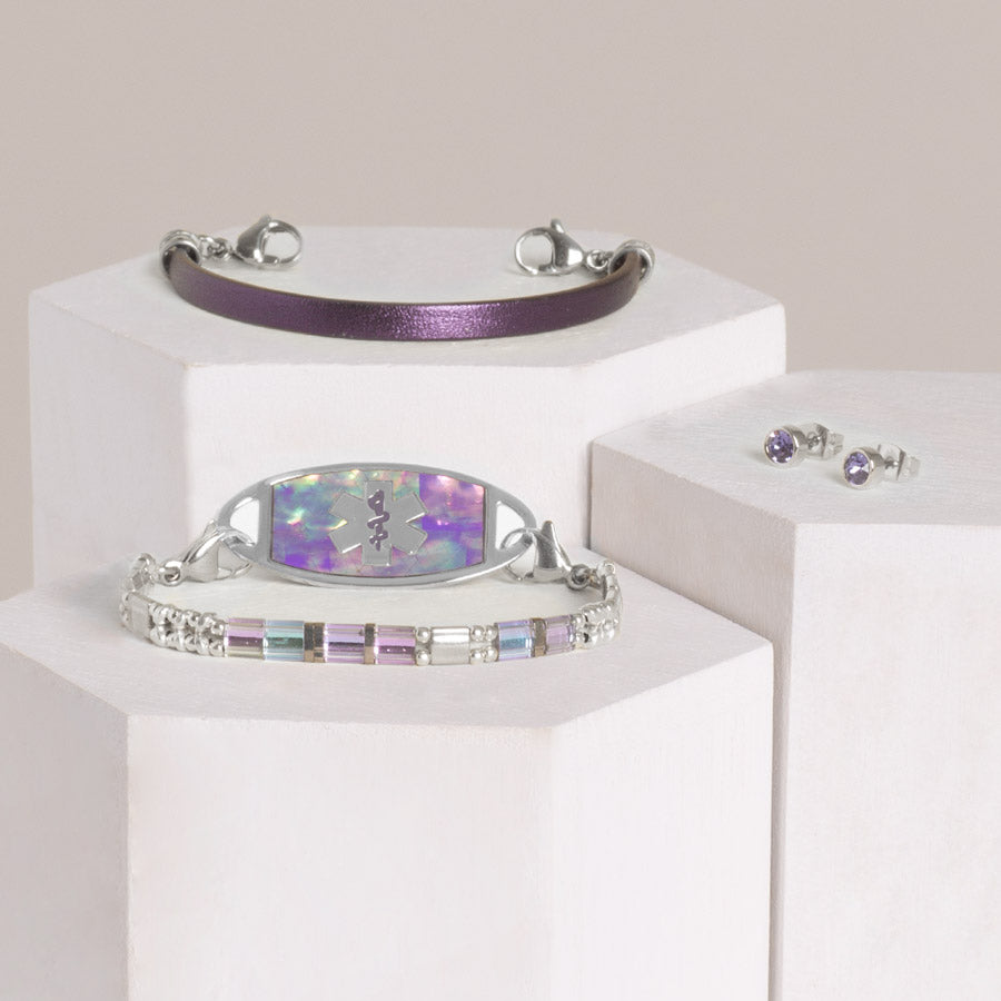 Silver and pastel beaded stretch bracelet with stainless steel lilac abalone inlay ID tag, metallic purple leather med ID band, and silver tone, round tanzanite cubic zirconia stud earrings on hexagon blocks.