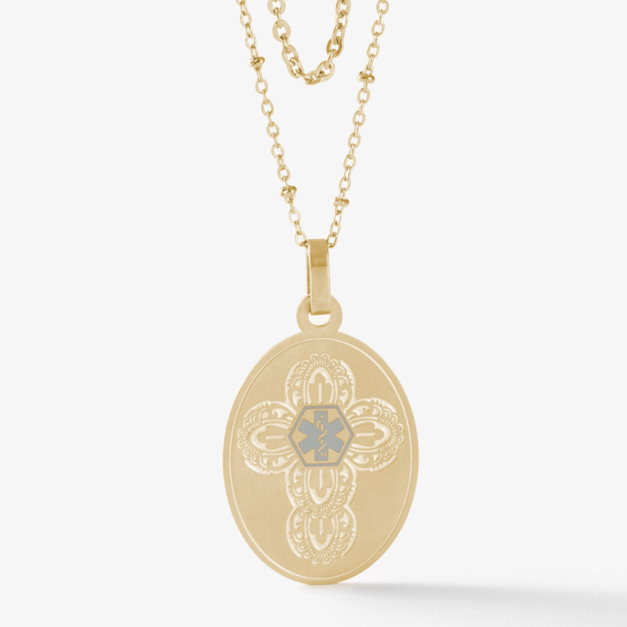 Gold tone oval pendent with detailed cross pattern and charcoal medical symbol on layered satellite and oval necklace chains.