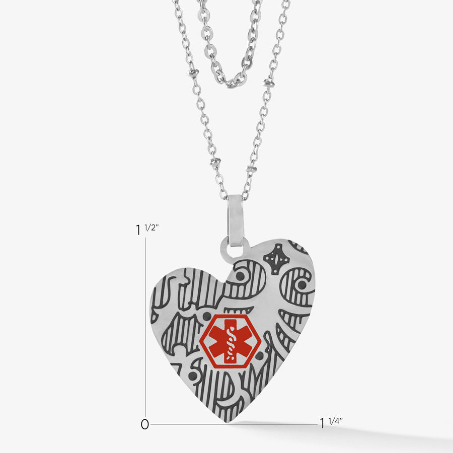 Measurements of silver heart pendant with decorative pattern with black inlay and red medical symbol on a layered necklace strand.