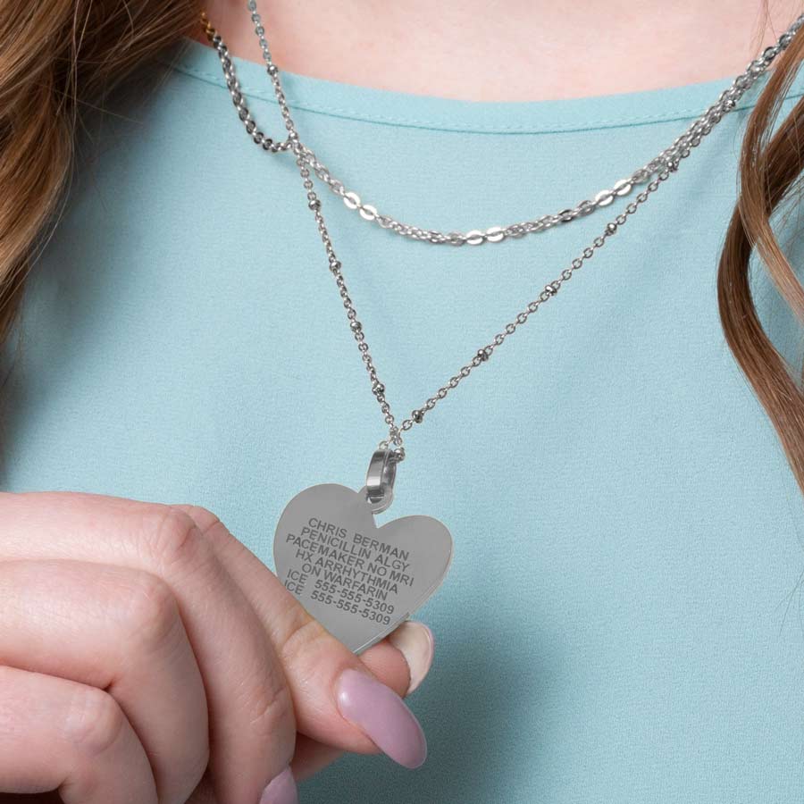 Woman wearing silver heart pendant necklace with premium laser engraving worn on layered necklace strands. 