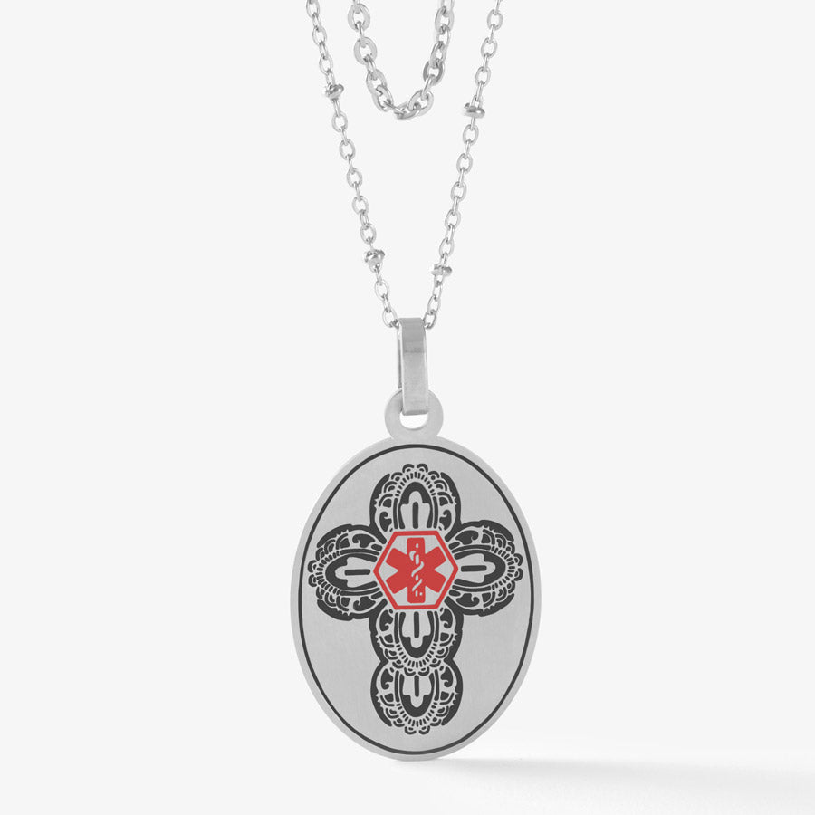 Vertical oval silver tone medical alert pendant with intricate cross detail and red medical symbol at center