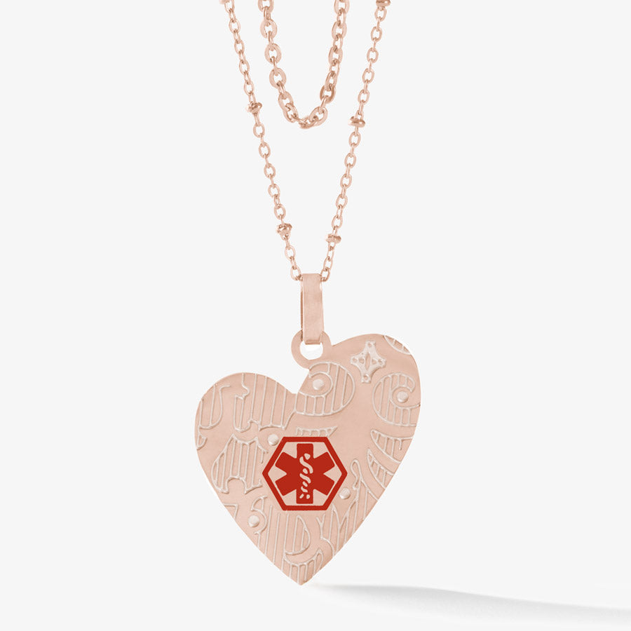 Rose gold tone stainless steel heart pendant on layered necklace chain with red medical symbol and pearl inlay on pattern.