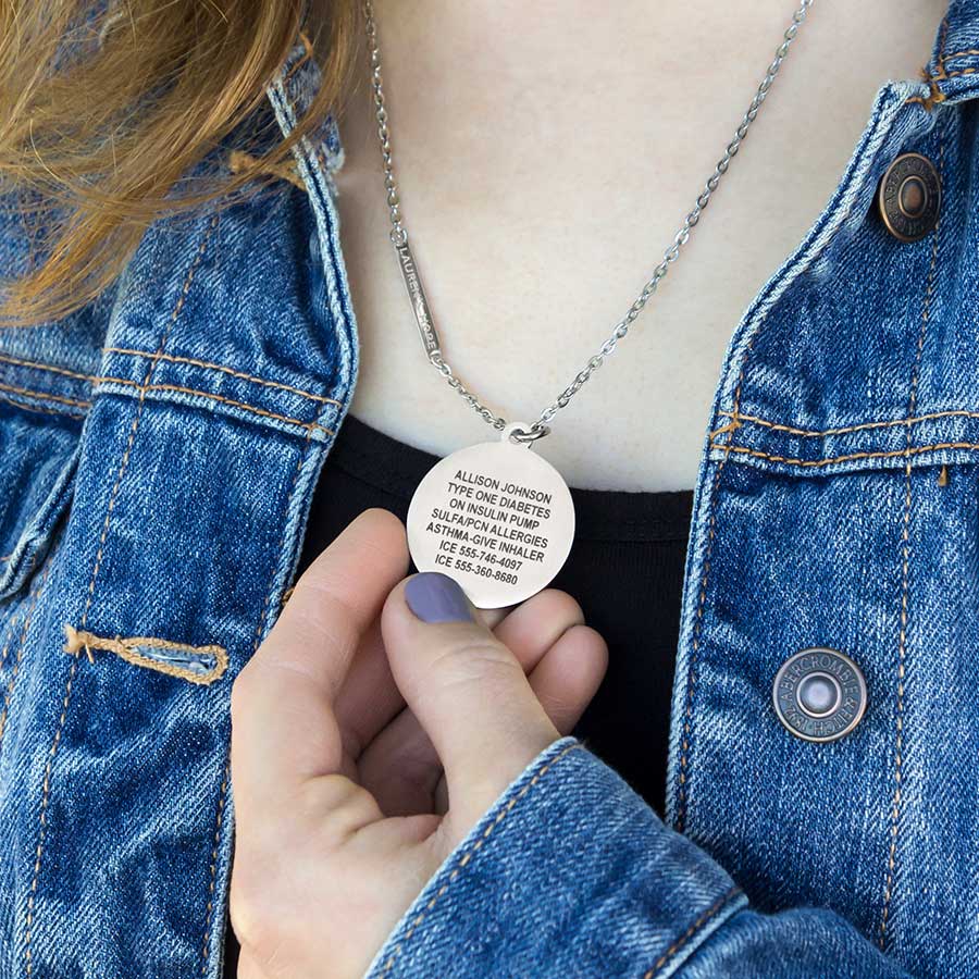 Woman wearing 1-1/4 inch round silver tone stainless pendant. Has engraving on the back. On flat oval chain with LH logo bar