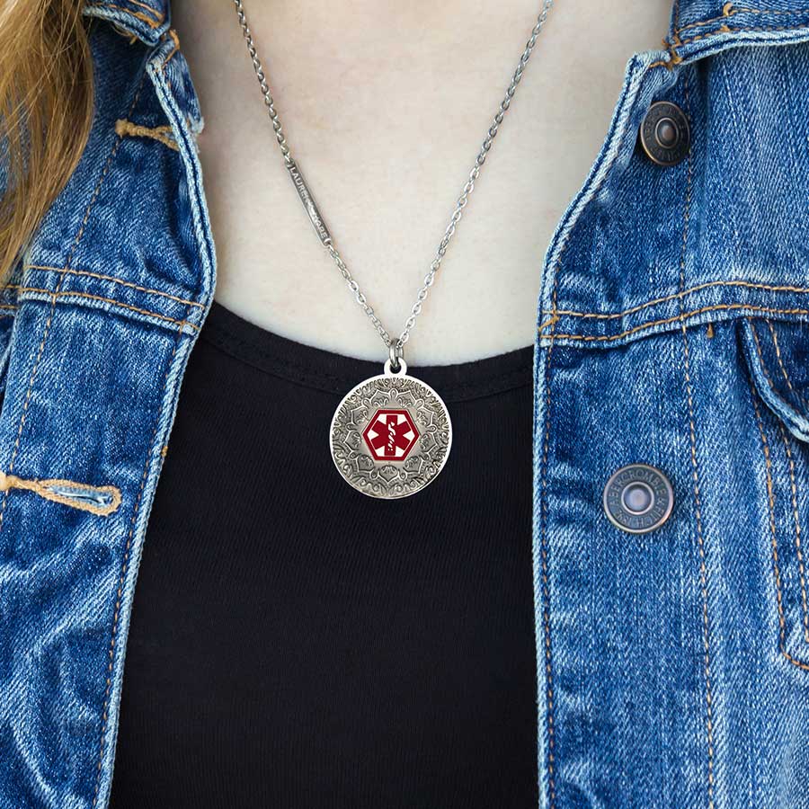 Woman wearing round silver tone stainless pendant with antique patina and clear layer over intricate pattern. Flat oval chain