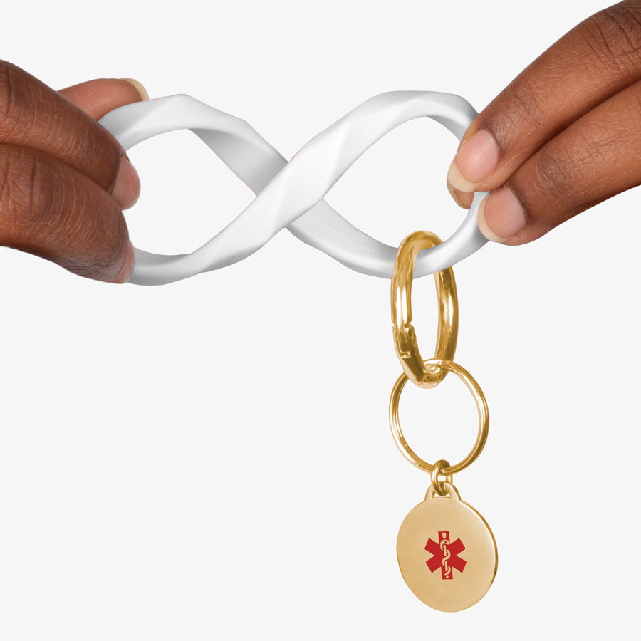 Woman twisting the white faceted silicone key ring wristlet with gold tone medical alert charm.