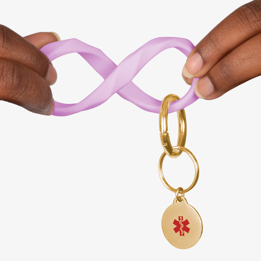 Woman twisting the lilac faceted silicone key ring wristlet with gold tone medical alert charm.