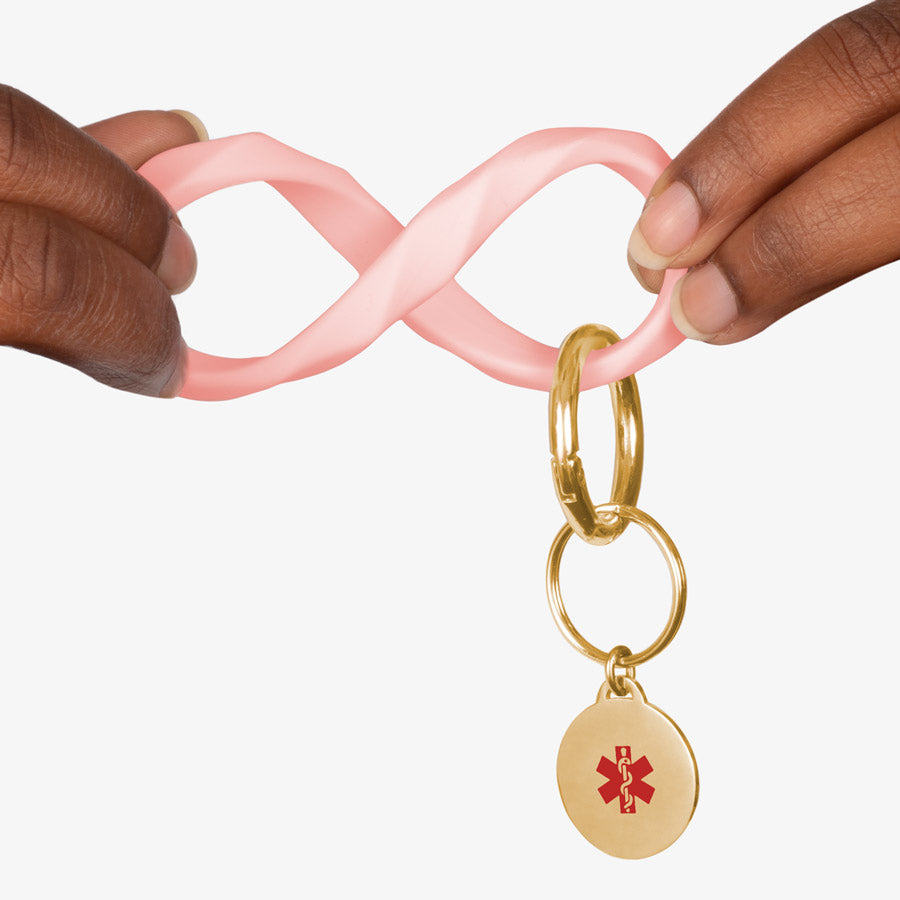 Woman twisting the soft pink faceted silicone key ring wristlet with gold tone medical alert charm.